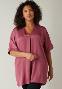 Blusa corta, a maniche corte, di colore bordeaux, realizzata in tessuto morbido con scollatura a V e fessure laterali, caratterizzata da una vestibilità comoda.