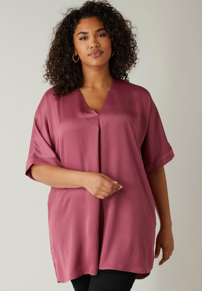 Blusa corta, a maniche corte, di colore bordeaux, realizzata in tessuto morbido con scollatura a V e fessure laterali, caratterizzata da una vestibilità comoda.