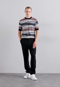 Svītrots īssvītra džemperis ar jūras zilo, sarkano un krēmkrāsas viļņiem; apvienots ar melnajām biksēm un baltajām kedām; gluda tekstūra, brīvs piegriezums.