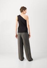 Top negro de un solo hombro hecho de una tela suave, combinado con pantalones de pierna ancha grises de talle alto. El conjunto se sitúa contra un fondo claro y neutral.