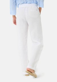 Pantalon en lin blanc à coupe décontractée, avec une jambe large, une taille élastique et une poche arrière unique. Associé à des espadrilles beige.