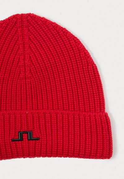Rode gebreide beanie met een geribbelde textuur, met een zwart logo-accent op de boord. Het ontwerp is strak en afgerond aan de bovenkant.