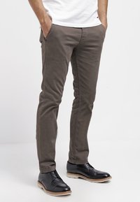 Graue Baumwollchinos mit schlanker Passform, ausgestattet mit Seitentaschen und einer glatten Textur, kombiniert mit schwarzen Lederschuhen und einem weißen T-Shirt.