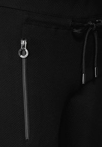 Svarta joggingsbyxor med en strukturerad väv, som har en silverfärgad dragkedja och midja med dragsko. Designen är sportig och funktionell.