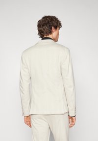 Lys beige blazer med en strukturert passform og subtil rutemønster, med svart krage og beige knapper på ermene.