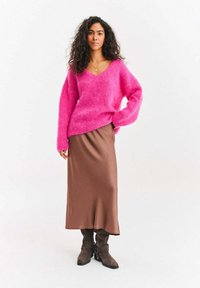 Różowy puszysty sweter z dekoltem w serek, zestawiony z brązową satynową midi spódnicą i brązowymi butami na sznurowadła, tworząc warstwową stylizację.