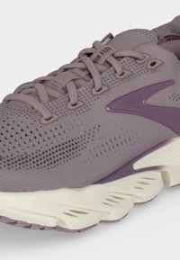 Gros plan d'une chaussure de running mauve avec une tige en mesh respirant, une semelle coussinée et un logo violet sur le côté.