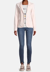Blazer rose clair ajusté avec revers crantés, deux boutons et poches avant, associé à un jean skinny bleu et des baskets beige.