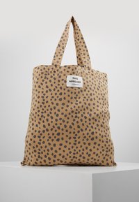 Beige tygväska med svarta oregelbundna fläckar och tyghandtag, med en vit etikett som läser "Mads Nørgaard Copenhagen."