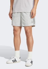 Hellgraue Sportshorts mit einem elastischen Bund, die an den Seiten drei vertikale Streifen und ein Logo auf der Vorderseite haben.