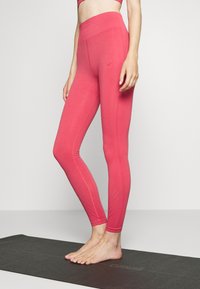 Legginsy z wysokim stanem, dopasowane, w intensywnym różowym kolorze z teksturowanymi akcentami i gładkim wykończeniem, noszone na boso na macie do jogi.