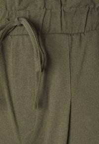 Pantalones jogger de algodón verde con cintura elástica, con cordón ajustable y bolsillos laterales. Tela texturizada con acabado suave y flexible.