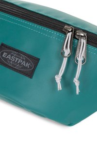 Pochette Eastpak in teal, realizzata in materiale testurizzato, presenta una patch nera con logo, zipper argentata con cordini grigi e forma rettangolare.