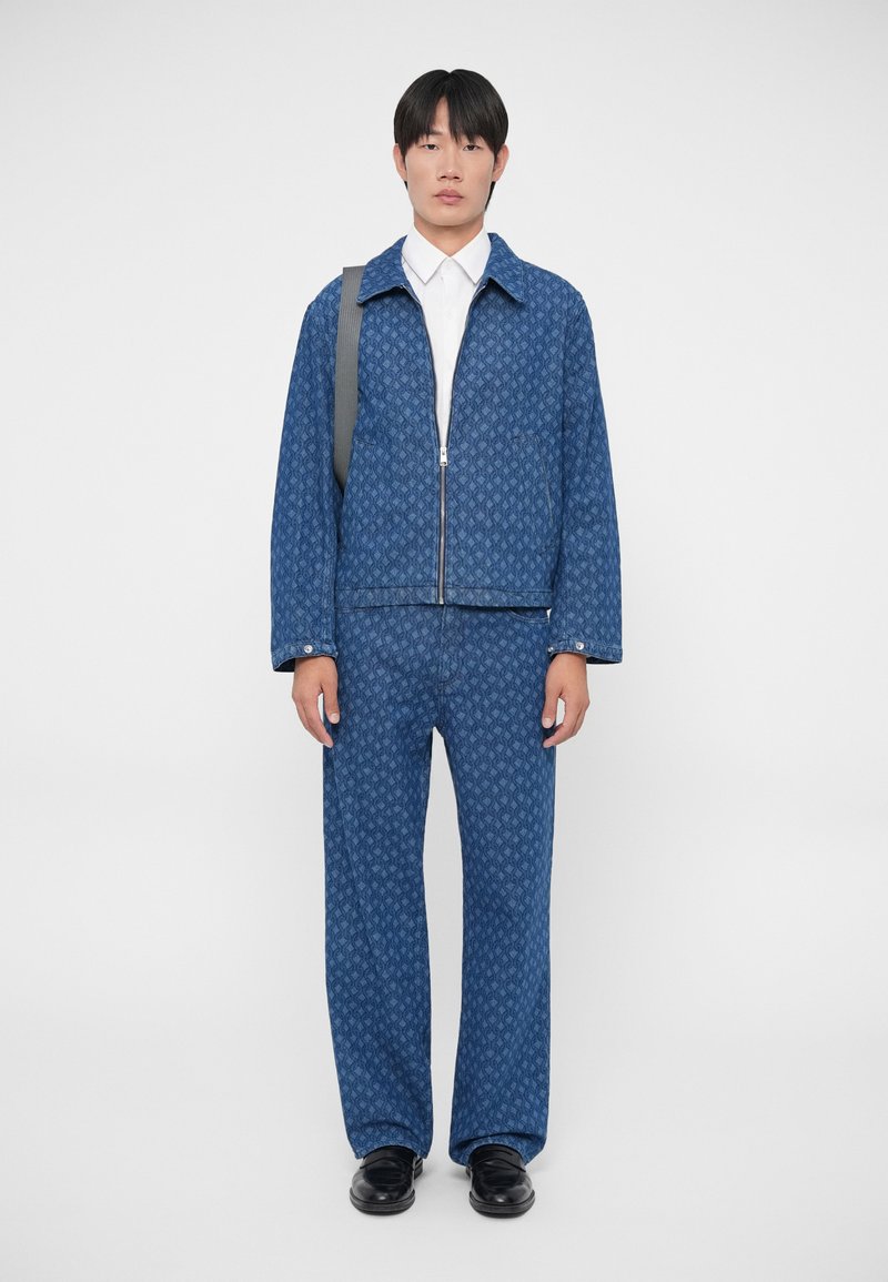 Blue patterned jacket with matching trousers, featuring a zip closure and collar. Smooth fabric, worn with a white shirt and black shoes.
