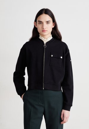 Black cropped sweatshirt with zip closure, rounded collar, and front pocket with snap button. Soft fabric and loose fit.
