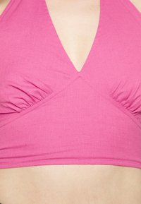 Top halter rosa com um decote em V profundo, detalhes franzidos nas laterais e uma textura suave. O tecido parece leve e macio.
