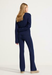 Svetle námořnická modrá pletená svetr s žebrováním a odpovídající rozšířené kalhoty, obojí s dlouhými rukávy a uvolněným střihem, doplněné o světlé hnědé obuv.