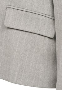 Grey blazer with a textured fabric, featuring a single pocket and subtle vertical stripes. The design includes clean lines and a tailored fit.