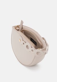 Pyöreä, beige käsilaukku, jossa on sileä nahkapinta, koristeellinen pyöreä olkahihna ja yksi vetoketjullinen tasku sisällä. Kultasävyiset metallidetaljit.