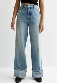 Jeans de tiro alto en azul claro, de pierna ancha y con un acabado deslavado, con dobladillos acurrucados y diseño tradicional de cinco bolsillos. Fabricados en material de mezclilla.