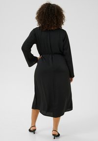 Vestido negro de manga larga con cintura ajustada y dobladillo a la rodilla. Tejido suave y ligero; la vista desde atrás muestra una silueta fluida y un escote sutil.