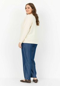 Cremfarbener Sweatshirt mit langen Ärmeln, kombiniert mit lockeren blauen Denim-Hosen und Ballerinas im Leopardenmuster. Schlichte Gestaltung, weicher Stoff.