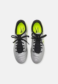 Nike Tiempo fodboldstøvler har en grå syntetisk overdel, sorte snørebånd og klare gule detaljer på indersiden og logoet. Glat tekstur, afrundet tå.