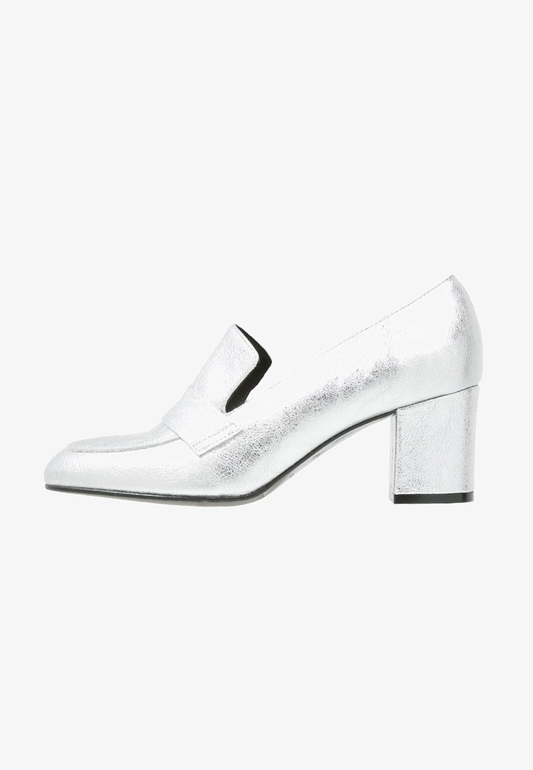 Mocassins à talon argenté avec une finition métallique lisse, un bout pointu et une large lanière sur le dessus. Talon carré pour la stabilité.