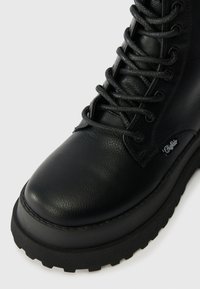 Melna ādas potīšu zābaki ar teksturētu virsmu, apaļu purngalu un biezu gumijas zoli. Iekļauj šņorējamu aizdari un nelielu zīmola detaļu.