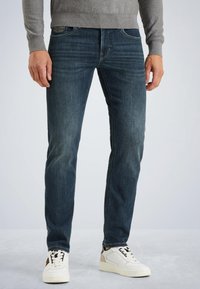 Donkerblauwe denim jeans met een rechte snit, met subtiele vervaging. Gecombineerd met witte sneakers, die contrasterende veters en accenten benadrukken.