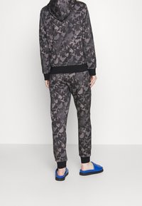 Felpa con cappuccio e pantaloni jogger in un motivo camouflage grigio scuro, con polsini e vita neri. Indossati con sandali a ciabatta blu.