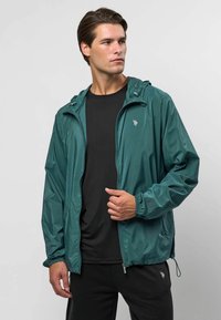 Waterdichte, gebreide jack in diep groenblauw met een rits aan de voorkant, elastische manchetten en een fitted zoom. Bevat een logo op de borst en een lichtgewicht stof.