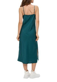 Zielona satynowa midi sukienka na ramiączkach, z bocznym rozcięciem i gładką fakturą, zestawiona z białymi, masywnymi sneakerami.