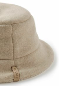 Beige fedorahatt i filt med rundad krona och bred, flexibel brätte. Har en liten, märkt etikett på sidan.