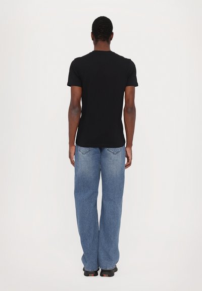 Svart bomull T-shirt med kort ärm, kombinerad med ljusblå denimjeans och svarta skor, sedd bakifrån mot en vit bakgrund.