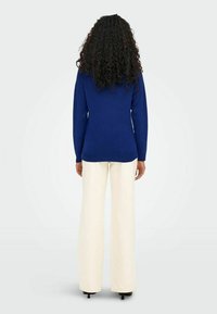 Kuning sinine, pika varrukaga sviiter otse lõikega, koos kreemi värvi laiade pükstega, mis näitavad sujuvat tekstuuri ja minimaalset detailide kasutust.