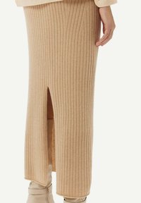 Stickad tan kjol med vertikal ribbad textur, med en slits på ena sidan, kombinerad med knähöga beige stövlar.