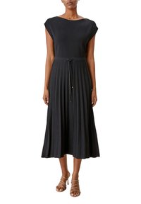 Donna che indossa un abito midi plisé senza maniche di colore nero con cintura regolabile in vita e sandali alti con cinturini color nude.