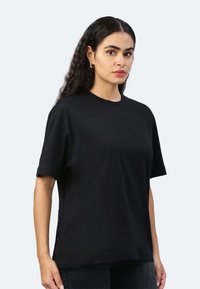 T-shirt nera a maniche corte in cotone con scollo girocollo e vestibilità rilassata, indossata da un modello contro uno sfondo chiaro.