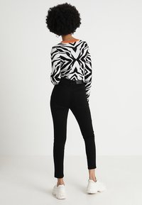 Vaqueros negros de cintura alta con una silueta ajustada combinados con un suéter de patrón en blanco y negro que tiene un cuello naranja. Zapatos blancos.