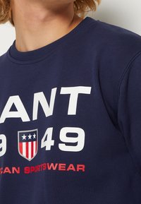 Marineblauwe sweatshirt met opvallende witte tekst "GRANT 1949" en een schildlogo met rode en witte strepen. Zachte stof met een ronde hals.