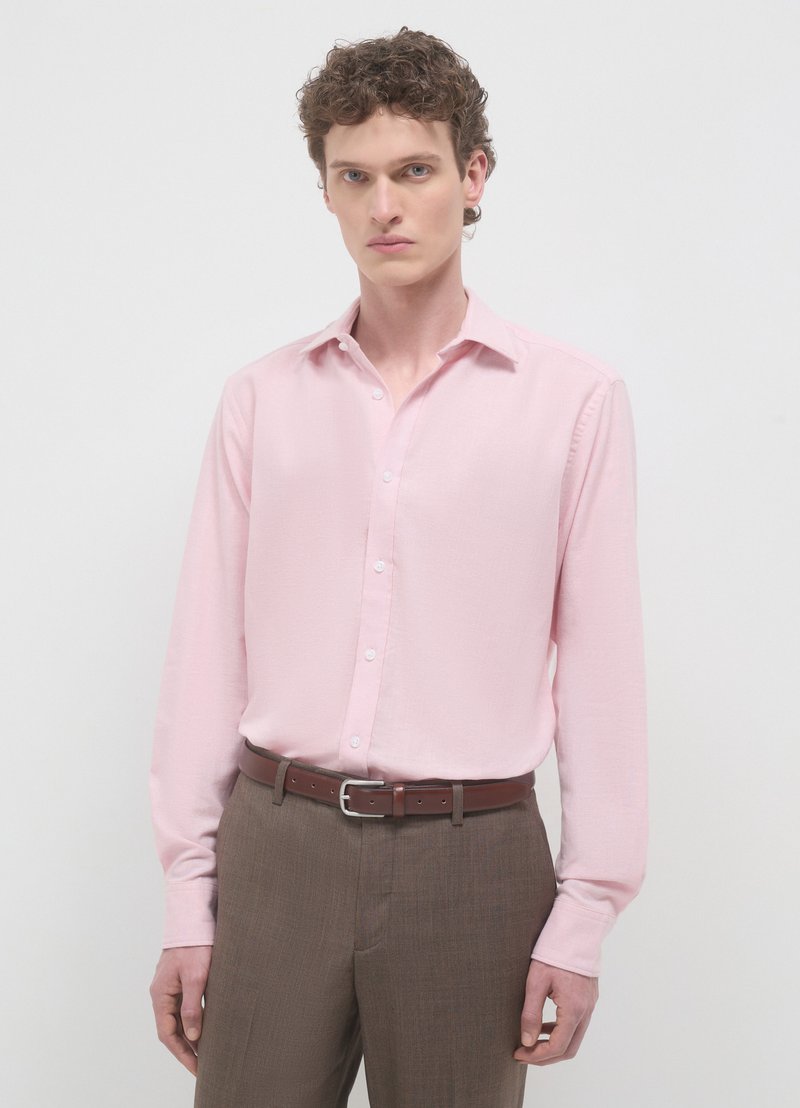 Hellrosa langärmliges Hemd mit spitzem Kragen und durchgehender Knopfleiste, kombiniert mit braunen Hosen und passendem Gürtel.