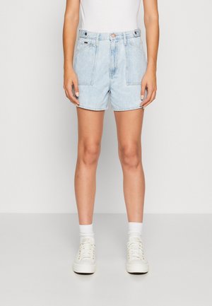 Shorts en denim bleu clair avec une taille haute, des poches avant et une fermeture à bouton. Associés à des baskets blanches et des chaussettes de cheville.