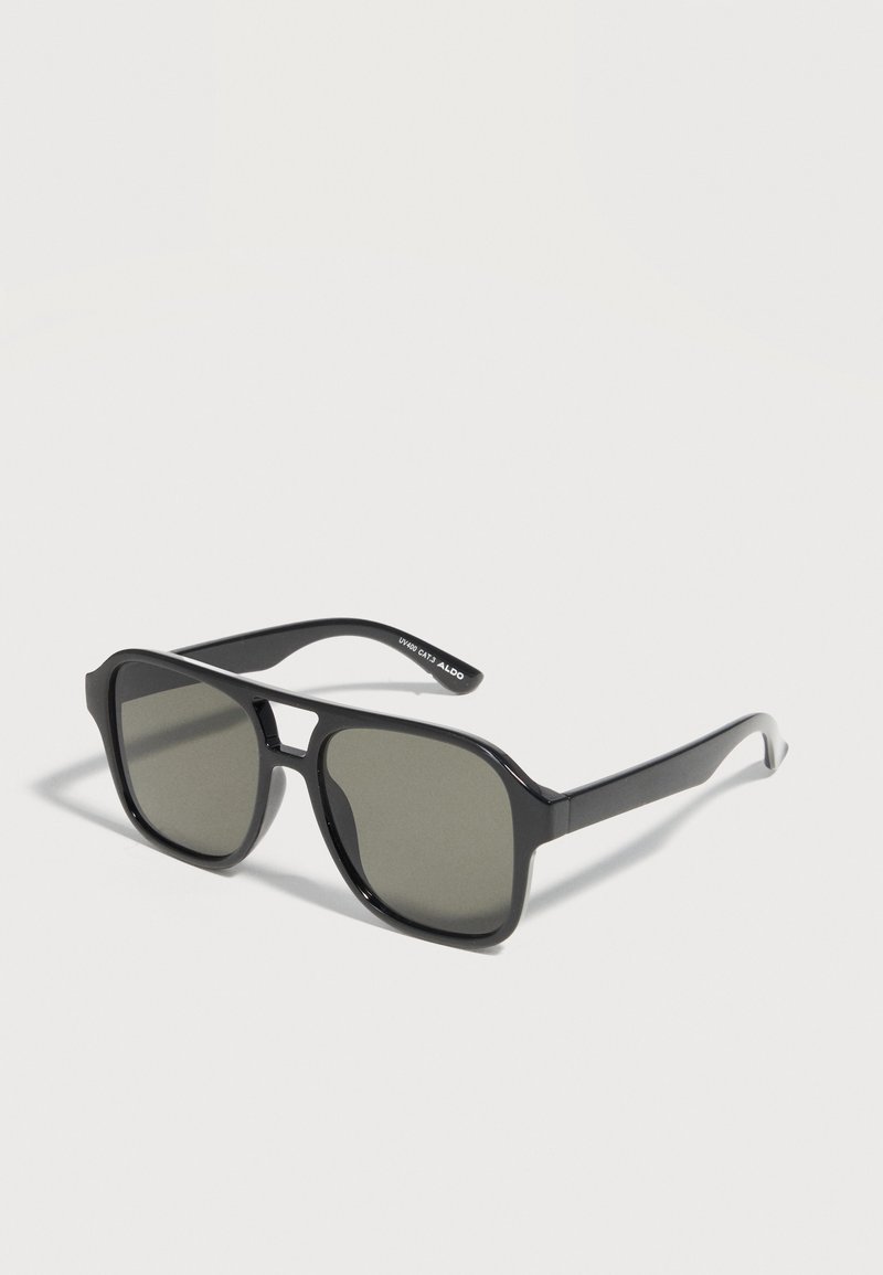 Lunettes de soleil rectangulaires noires avec des verres teintés foncés et une monture fine reposant sur une surface claire.