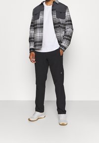 Rutig skjorta i svart och grått med två bröstfickor, kombinerat med svarta byxor och vita sneakers. Slät textur och avslappnad design.