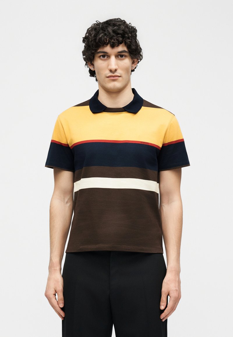 Man with curly dark hair wearing a short-sleeve polo shirt with yellow, navy, red, white, and brown horizontal stripes.