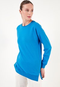 Sudadera azul de manga larga con cuello redondo, cortes laterales y puños y dobladillo acanalados. Confeccionada con un tejido suave, presenta un corte relajado.