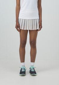 Falda de tenis blanca de malla con diseño ligero y plisado. Combinada con zapatillas negras con acentos en menta y calcetas deportivas blancas.