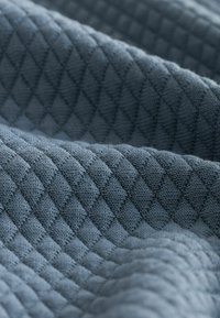 Tejido texturizado y acolchado en azul grisáceo oscuro. Presenta un patrón de diamante con una textura suave y tejida, creando profundidad y dimensión.
