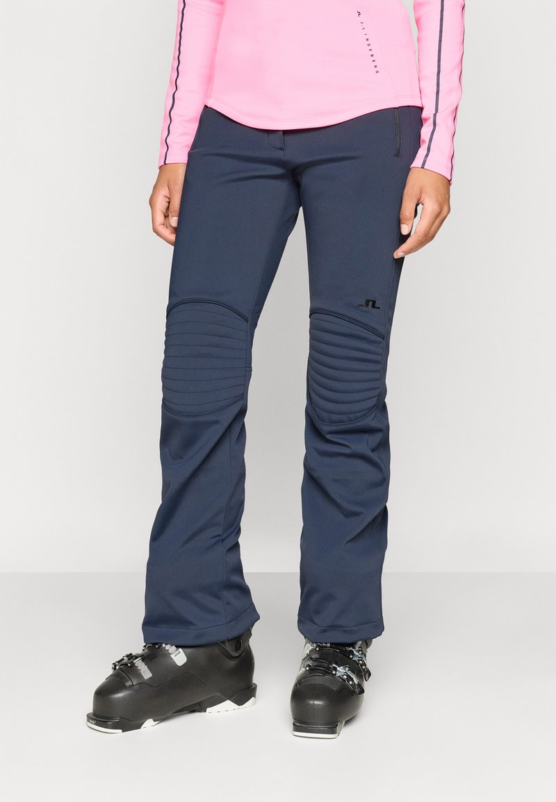 Námořnické lyžařské kalhoty s texturovanými kolenními panely a slim fit. Nosené s černými lyžařskými botami; mají minimalistické logo na stehně.